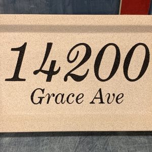 Two-line engraved address stone displaying house number and street name, mounted on a brick exterior.